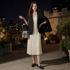 Woman in a black blazer and white dress standing on a rooftop at night with cityscape in the background