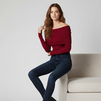 Woman wearing a red sweater and blue jeans sitting on a white couch against a light gray background
