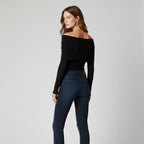 Woman wearing a black off-shoulder top and dark blue jeans on a light gray background