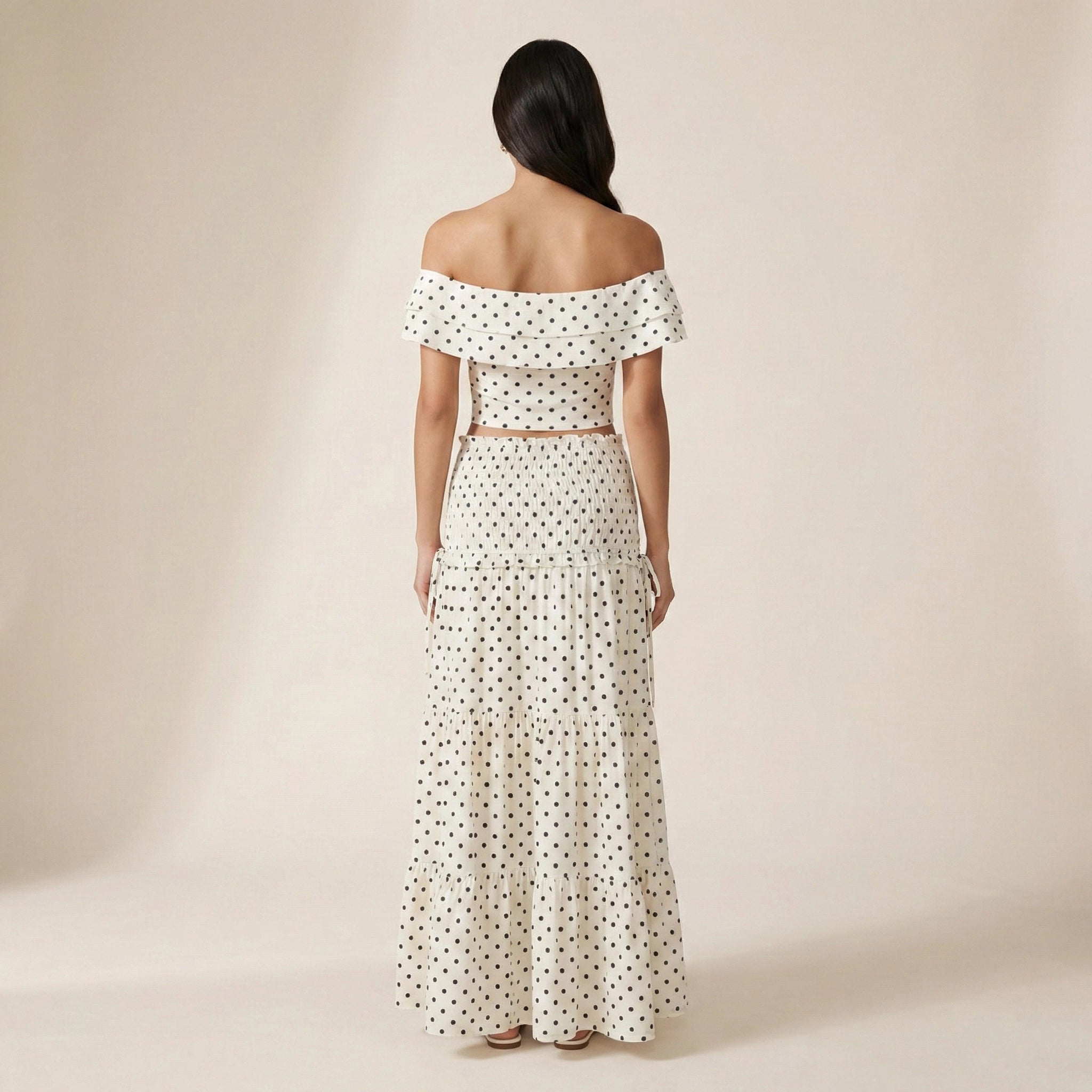 Woman wearing a polka dot off-shoulder top and long skirt set on a beige background
