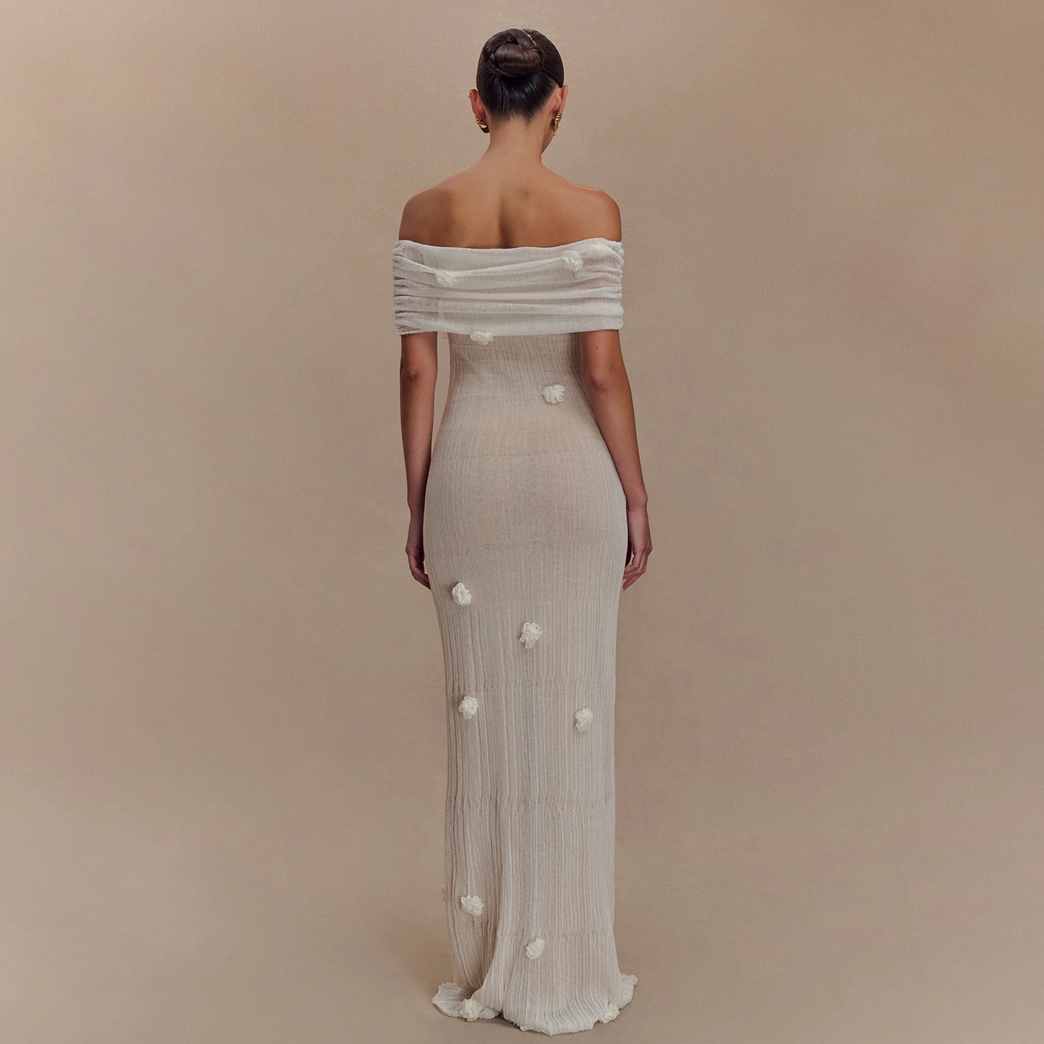 Woman wearing a long, off-shoulder dress with floral details on a beige background
