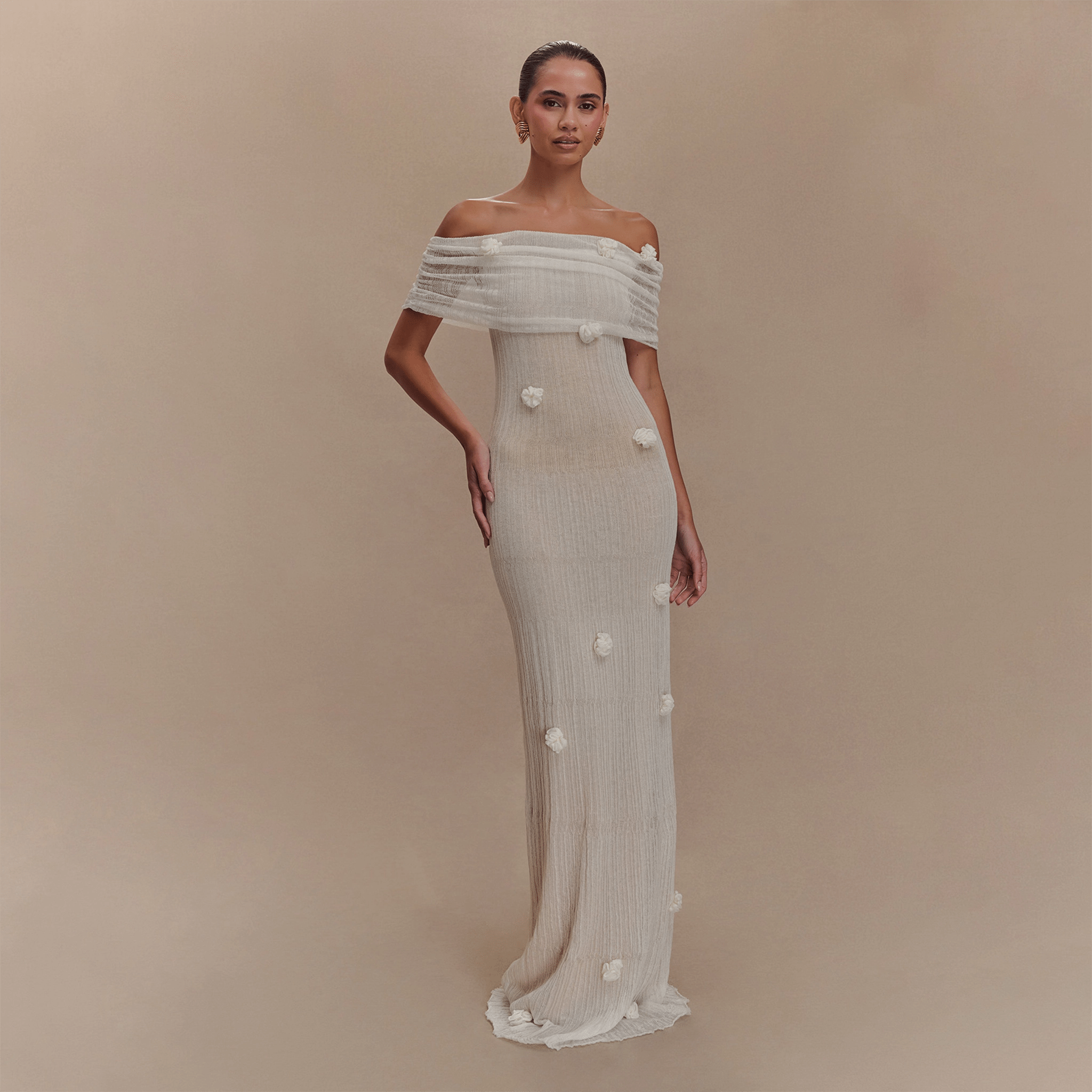 Woman wearing a white off-shoulder gown with floral details on a beige background