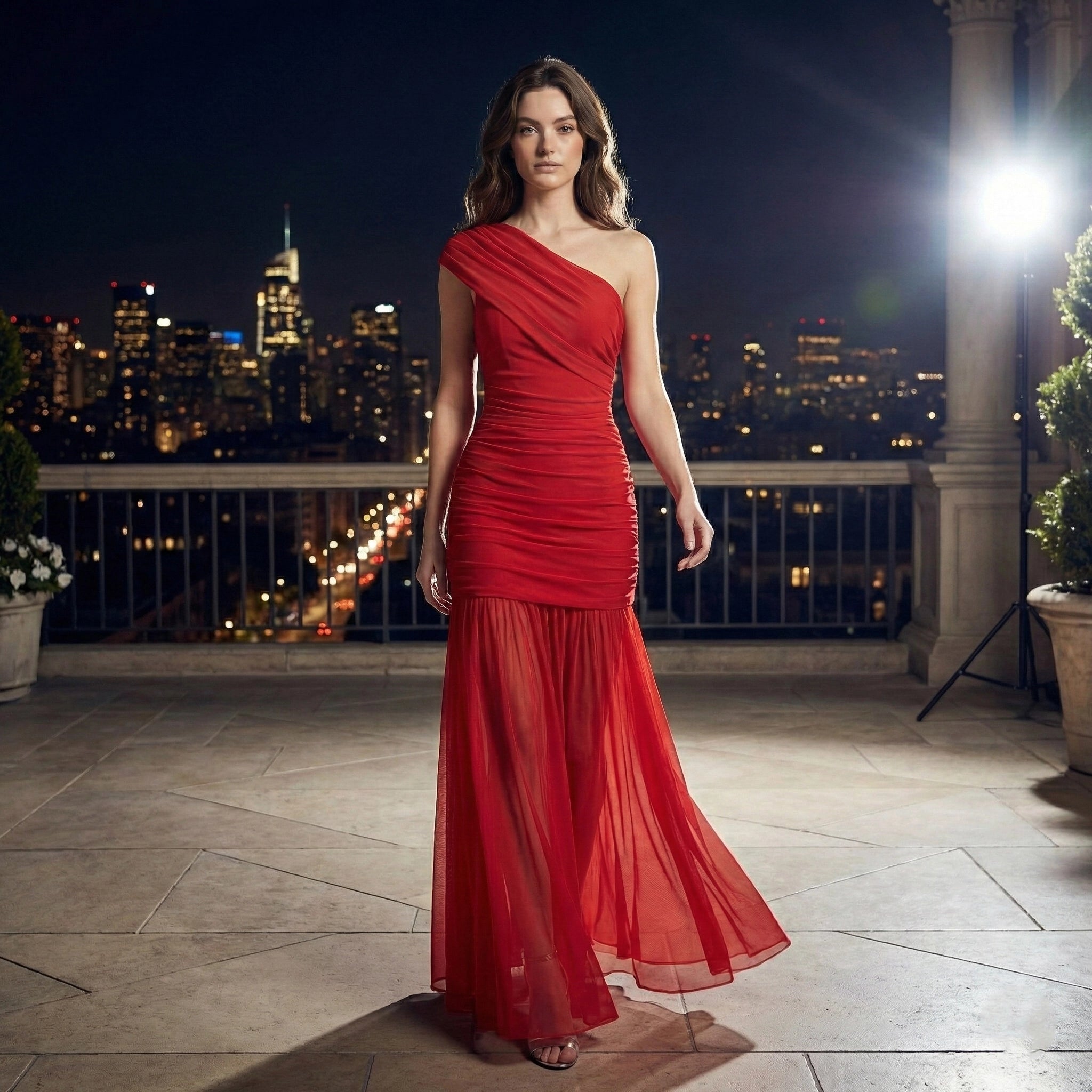 Woman in a red one-shoulder dress standing on a rooftop with a cityscape background