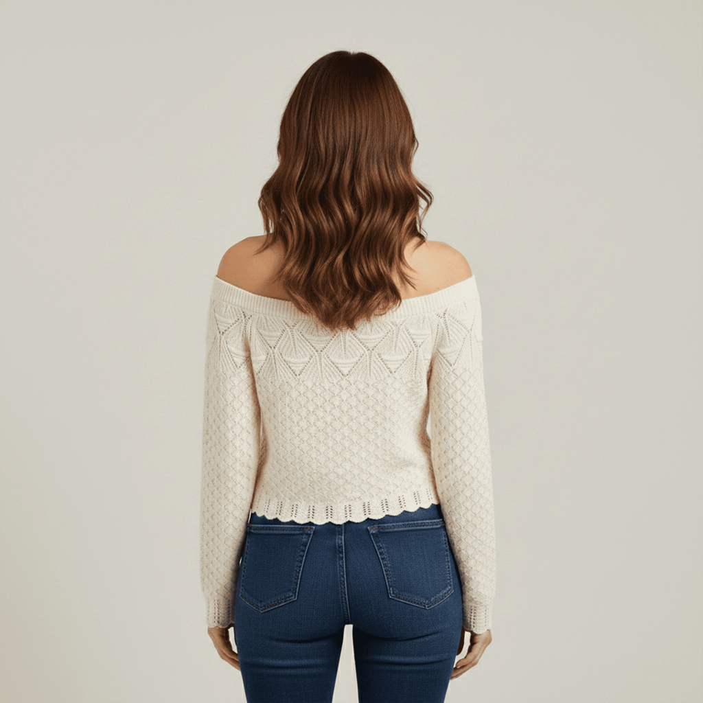 Woman wearing a cream off-shoulder sweater and blue jeans on a plain background