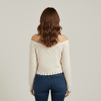 Woman wearing a cream off-shoulder sweater and blue jeans on a plain background