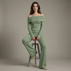 Woman wearing a green off-shoulder outfit sitting on a stool against a plain background