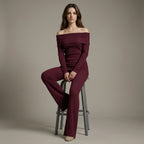 Woman wearing a burgundy off-shoulder outfit sitting on a stool against a plain background