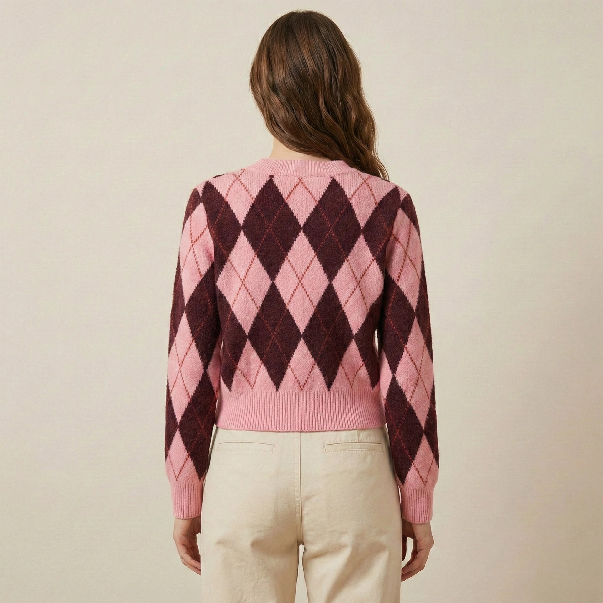 Person wearing a pink and brown argyle sweater on a beige background