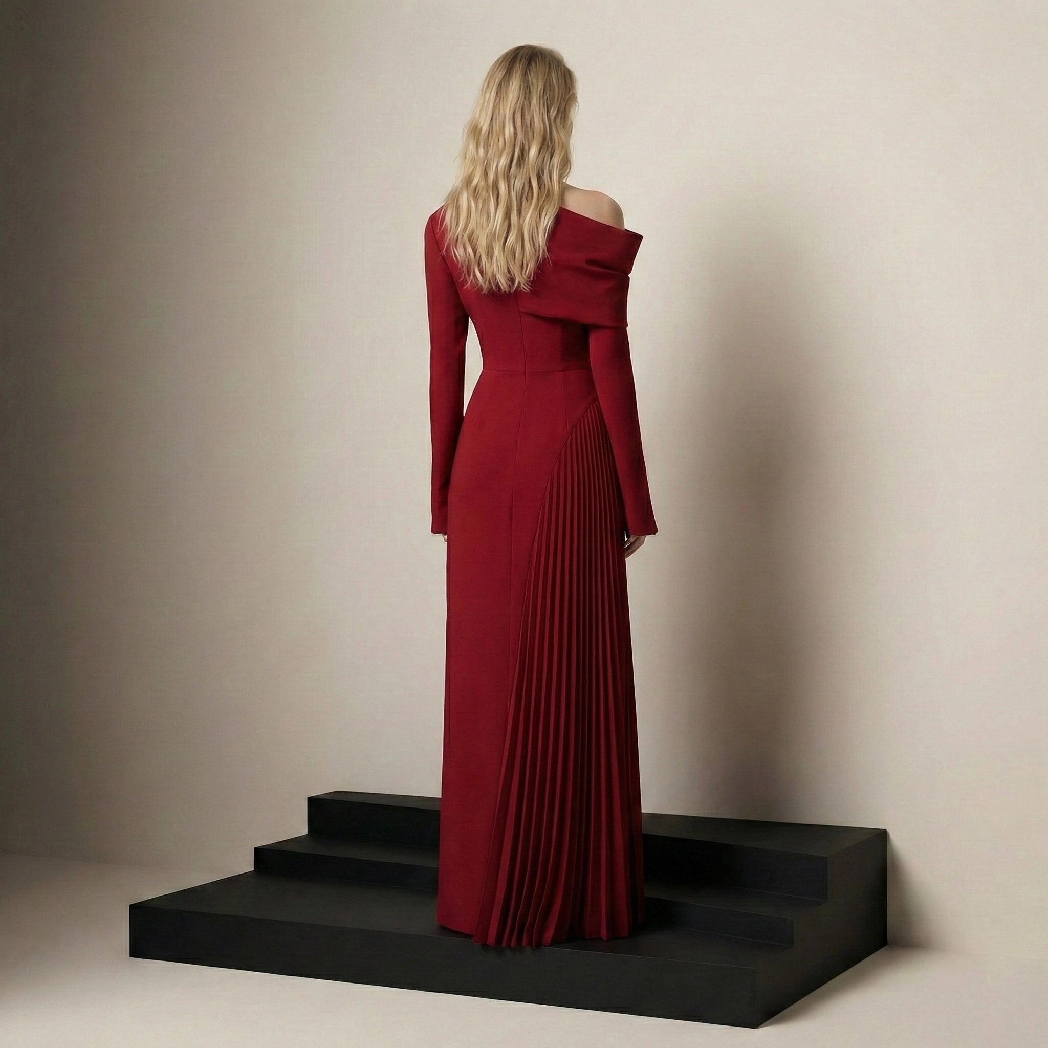 Woman in a red off-shoulder dress standing on black steps against a beige wall.