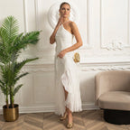 Woman in a white dress standing in an elegant room with decorative wall paneling and a plant.