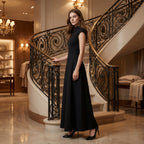 Woman in a black dress standing in a luxurious interior setting with a staircase.