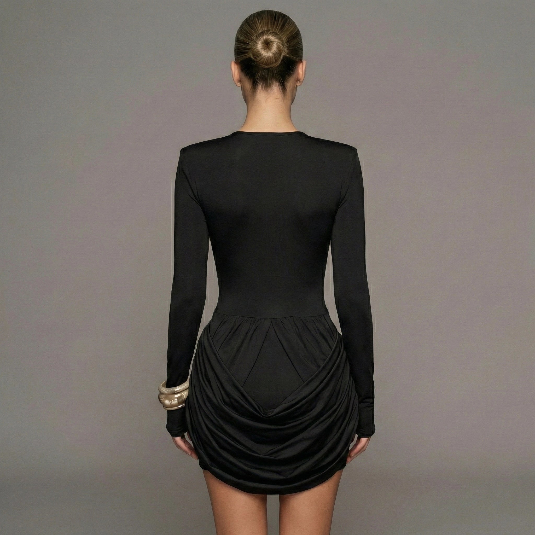 Black dress with long sleeves and a ruched skirt on a gray background