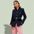 Woman wearing a navy blazer with gold buttons and pink pants on a light green background