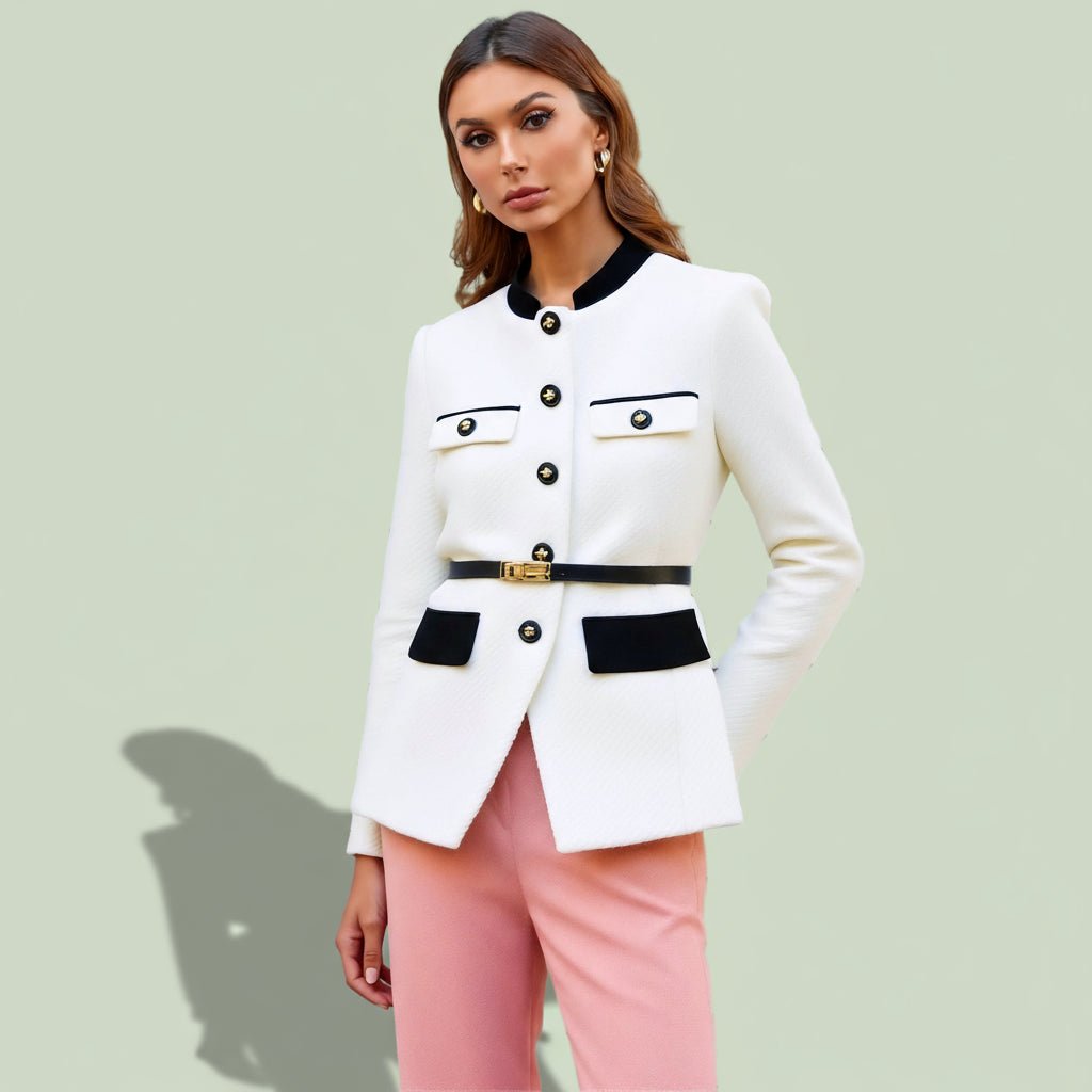 Woman wearing a white blazer with black accents and pink pants on a light green background