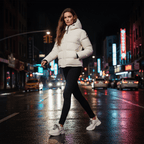Woman in a white puffer jacket walking on a city street at night.