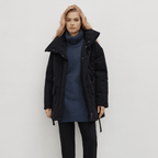 Woman wearing a black coat over a blue sweater on a white background