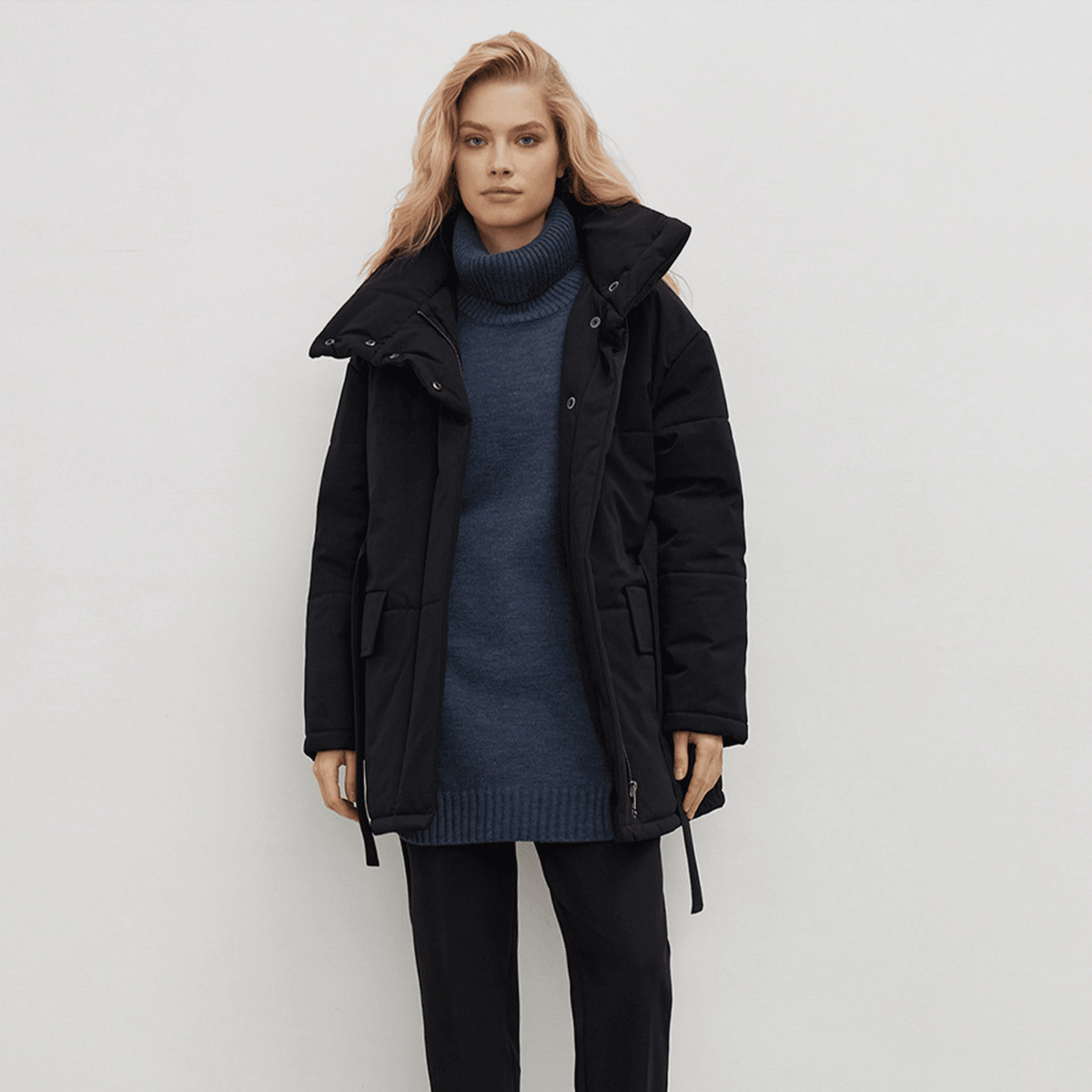 Woman wearing a black coat over a blue sweater on a white background