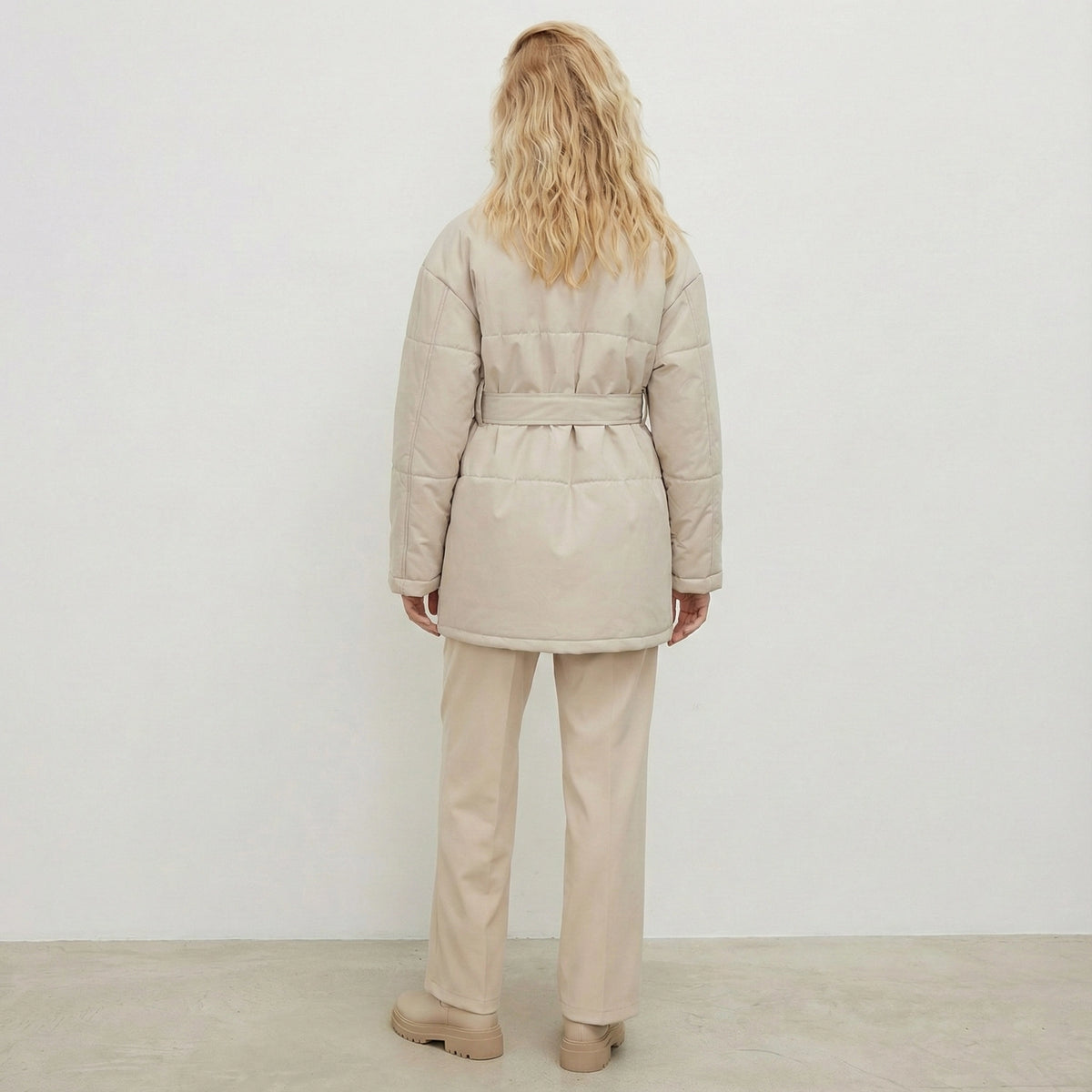 Person wearing a beige puffer coat and pants against a white background