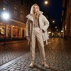 Woman in a beige coat standing on a cobbled street at night.