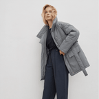 Woman wearing a gray coat and dark pants against a white background
