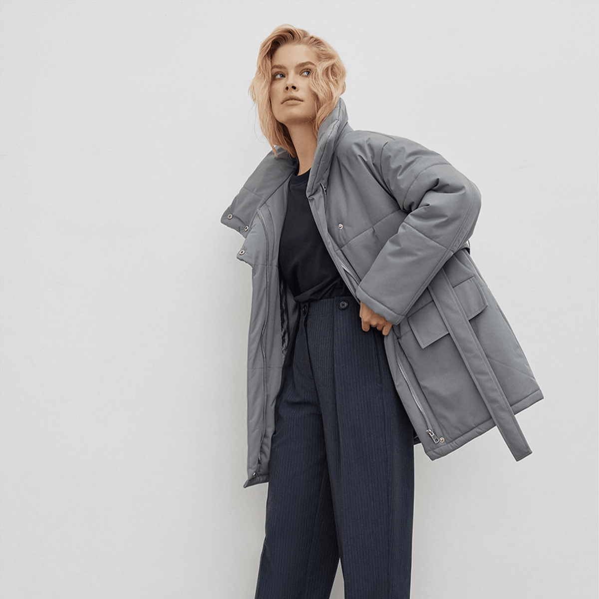 Woman wearing a gray coat and dark pants against a white background