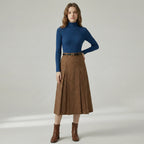 Woman wearing a blue turtleneck and brown skirt on a plain background