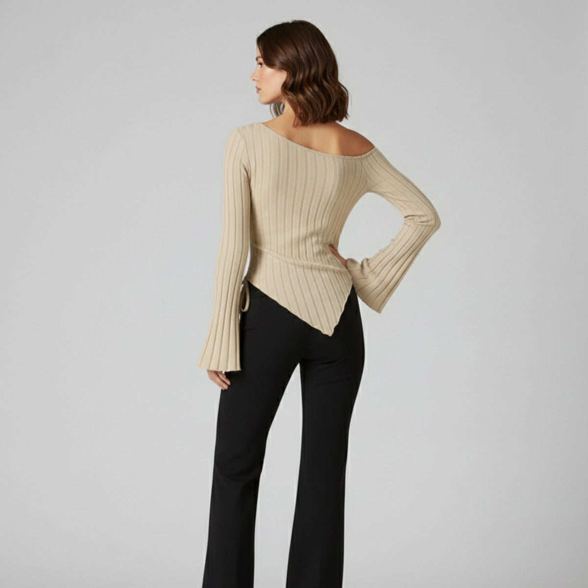 Woman wearing a beige ribbed sweater and black pants on a gray background