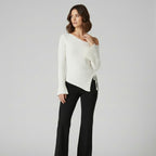 Woman wearing a white off-shoulder sweater and black pants on a light gray background