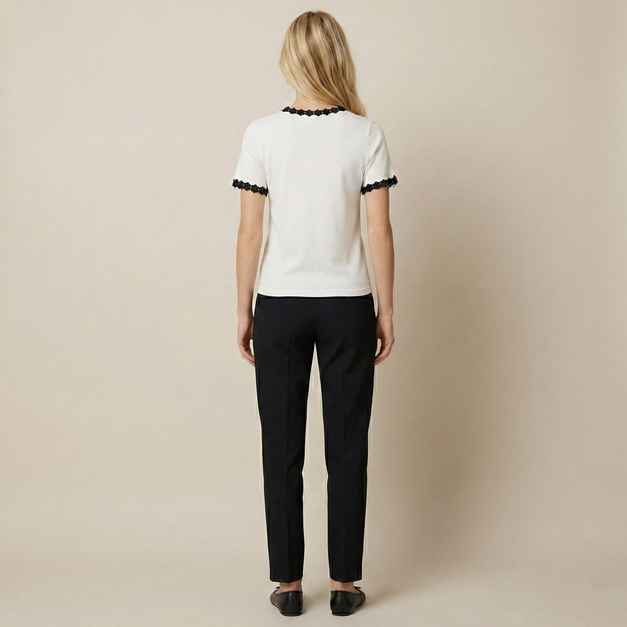 Woman wearing a white blouse with black trim and black pants on a beige background