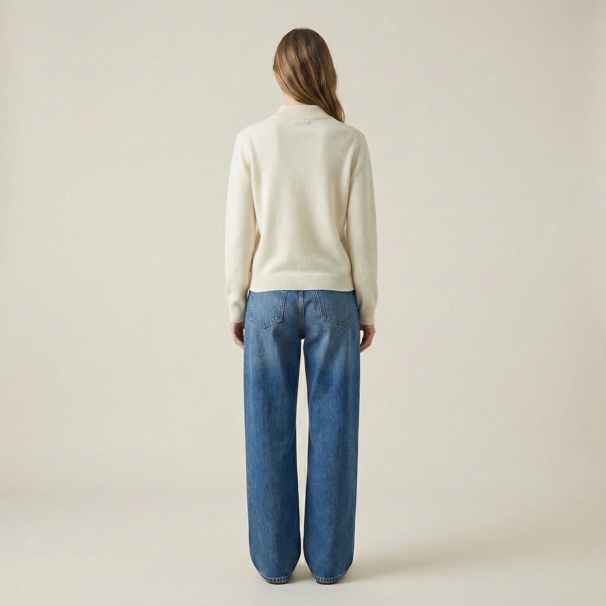 Person wearing a cream sweater and blue jeans on a beige background