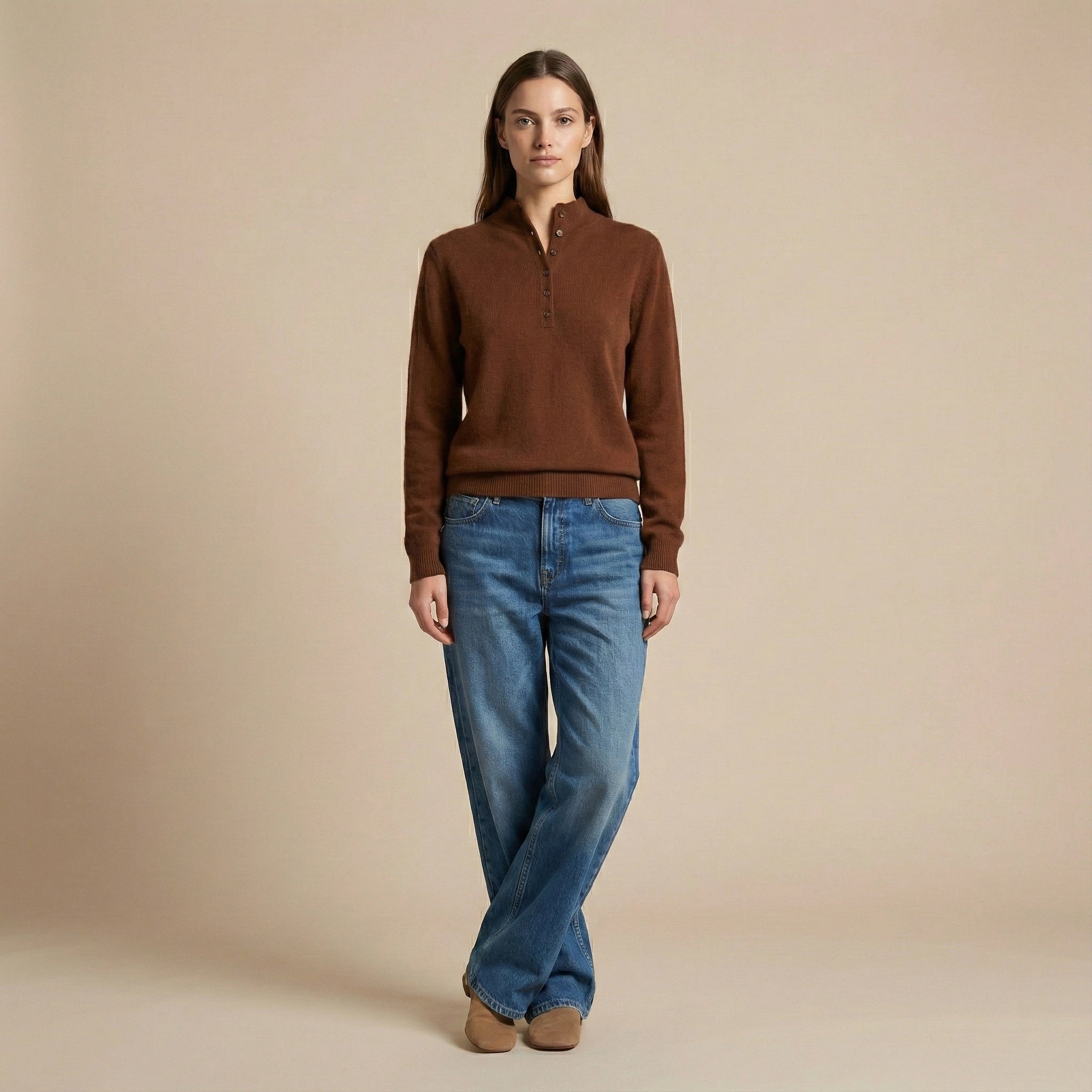 Woman wearing a brown sweater and blue jeans against a beige background