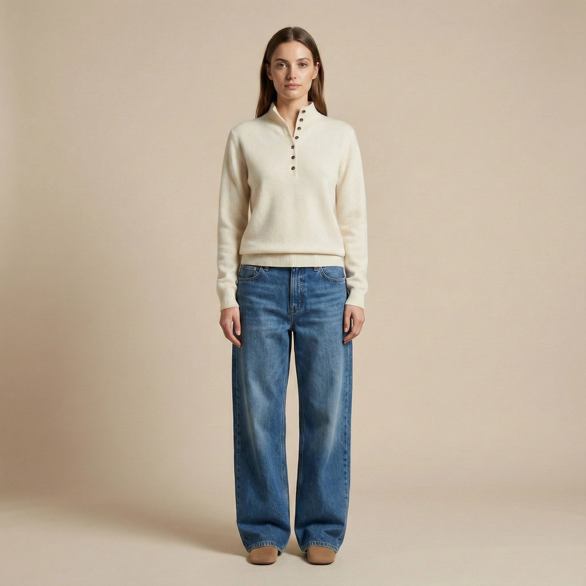 Woman wearing a cream sweater and blue jeans against a beige background