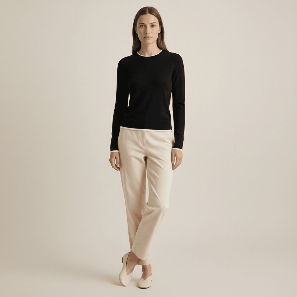 Woman wearing a black long-sleeve top and beige pants on a plain background