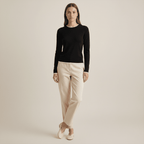 Woman wearing a black long-sleeve top and beige pants on a plain background