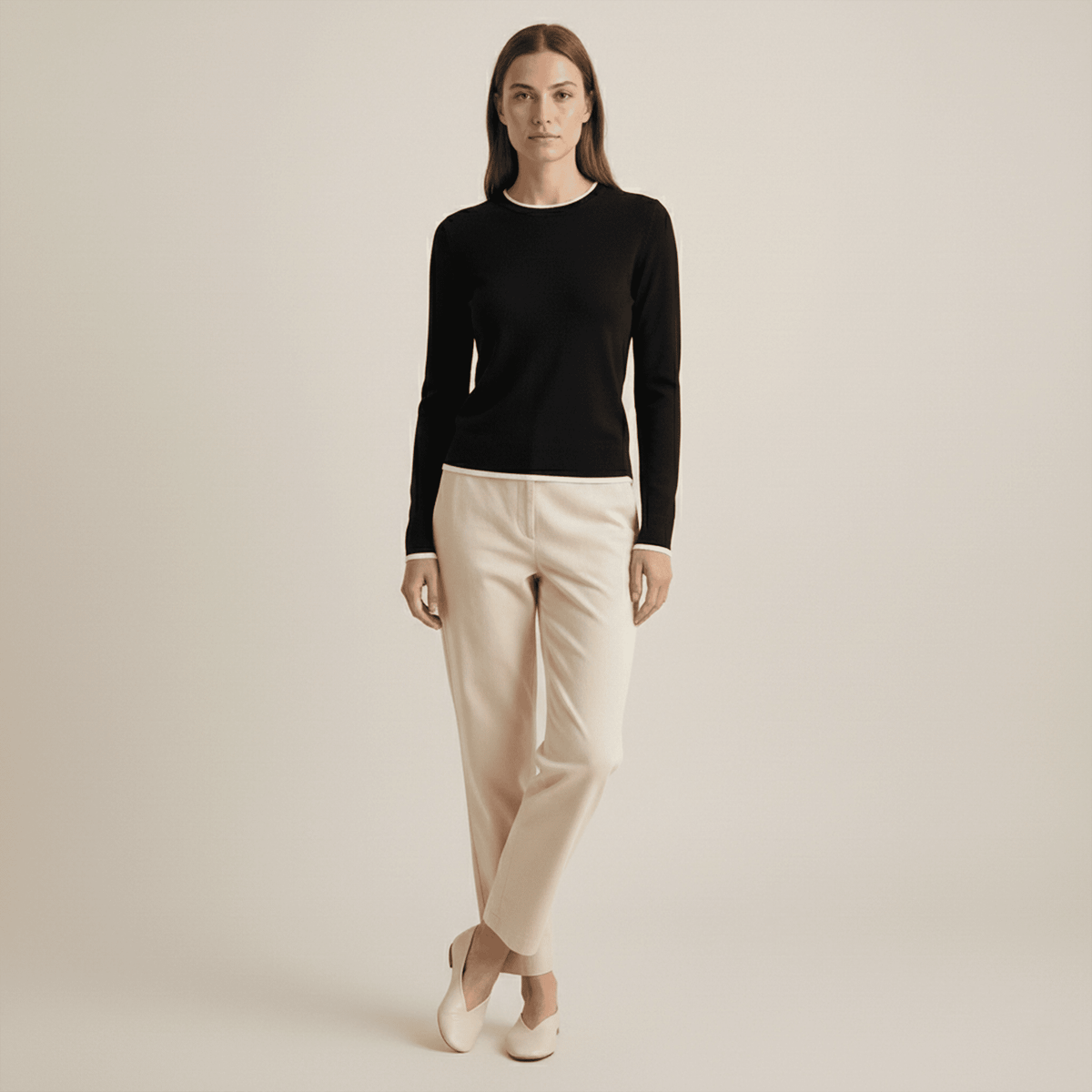 Woman wearing a black long-sleeve top and beige pants on a plain background