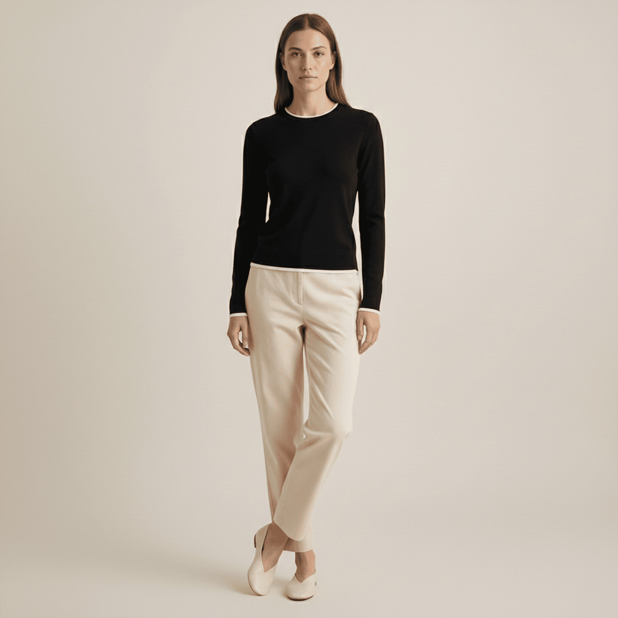 Woman wearing a black long-sleeve top and beige pants on a plain background
