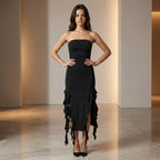 Woman wearing a black strapless dress with ruffled details in a neutral setting