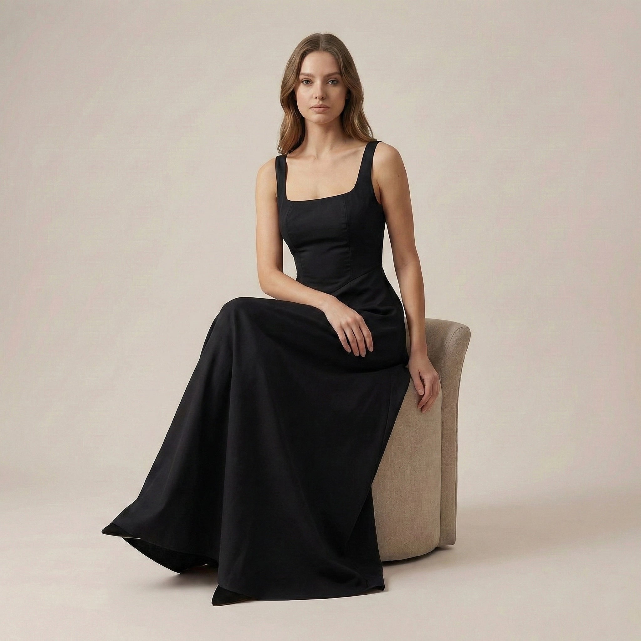 Woman wearing a black dress sitting on a beige chair against a neutral background