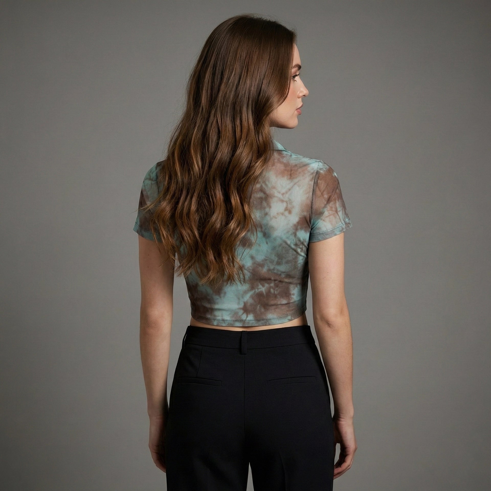 Woman wearing a tie-dye top and black pants against a gray background