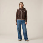 Woman wearing a brown sweater with white trim and blue jeans on a beige background