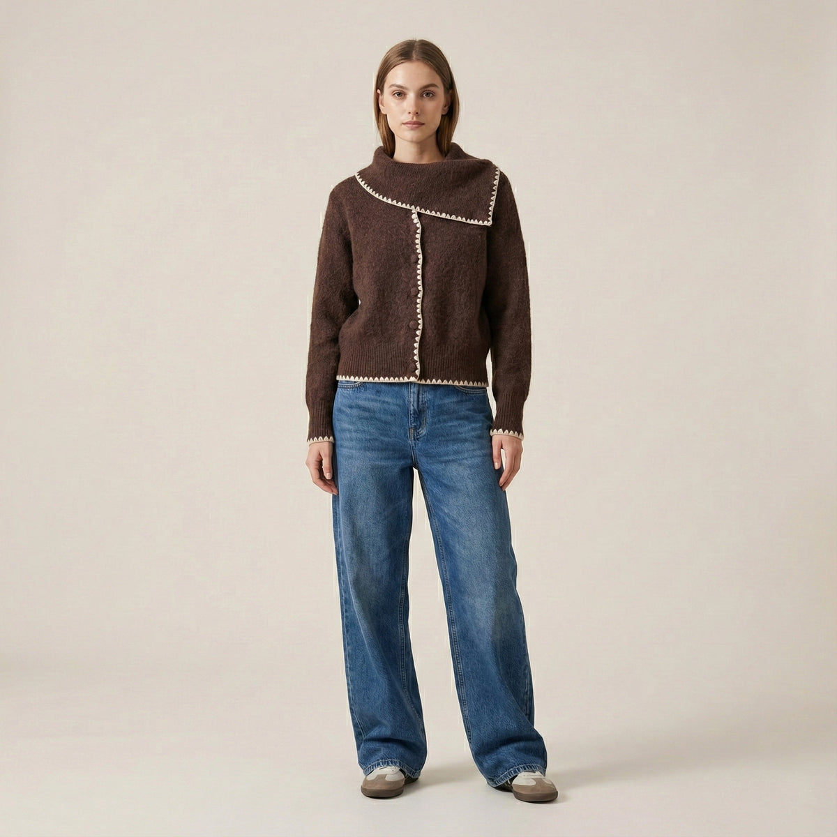 Woman wearing a brown sweater with white trim and blue jeans on a beige background