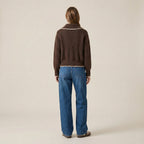Person wearing a brown sweater and blue jeans on a beige background