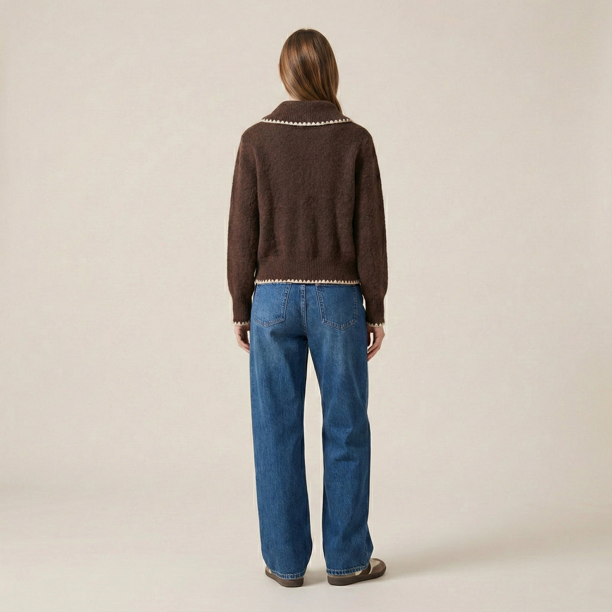 Person wearing a brown sweater and blue jeans on a beige background