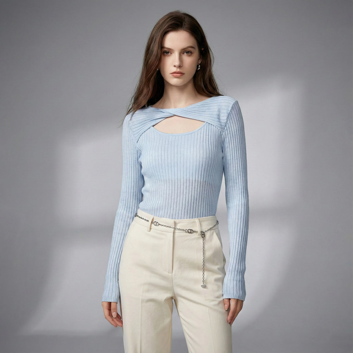 Woman wearing a light blue ribbed sweater and beige pants on a gray background