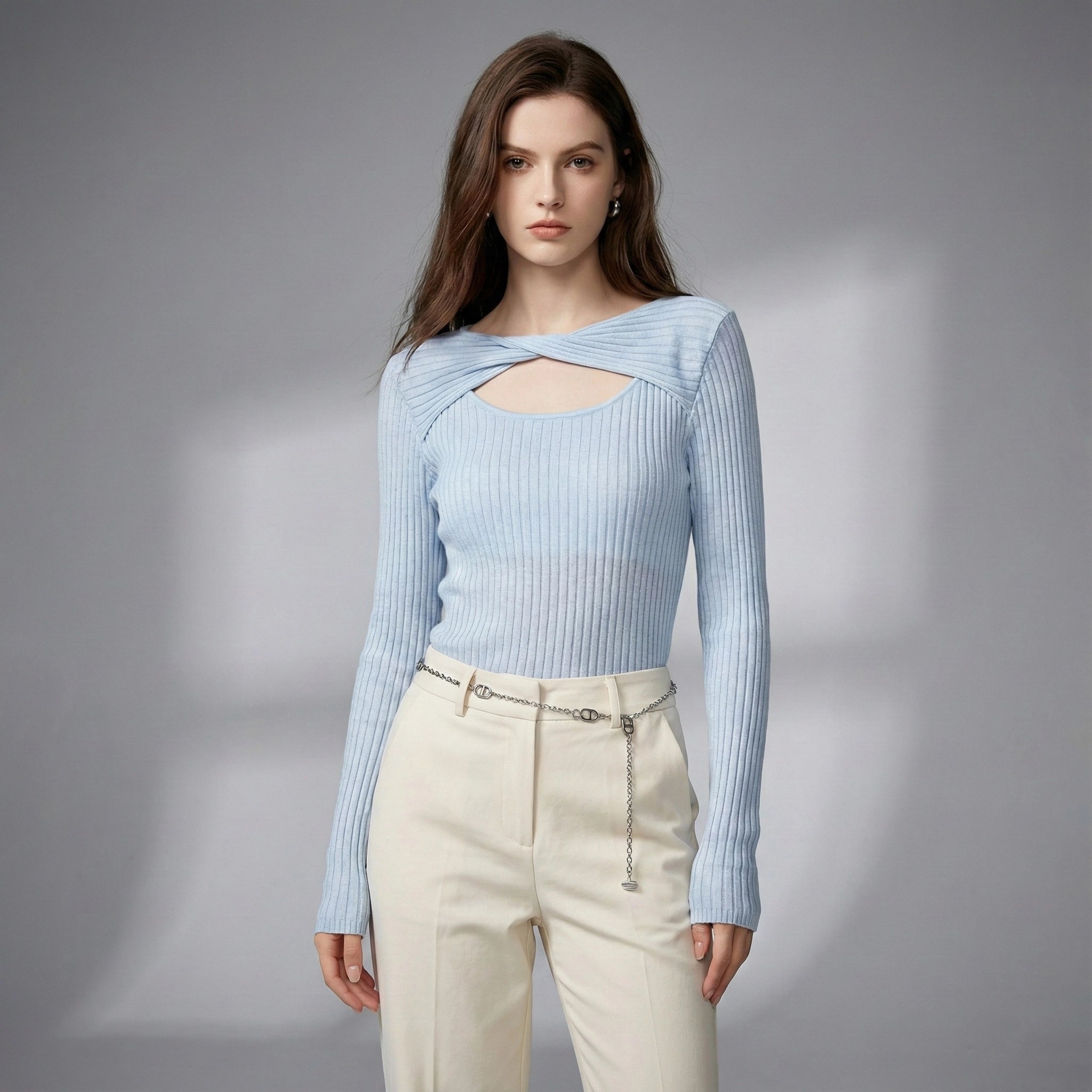 Woman wearing a light blue ribbed sweater and beige pants on a gray background
