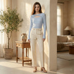 Woman in a light blue top and beige pants standing in a bright living room.
