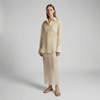 Woman wearing a beige shirt and pants on a plain background