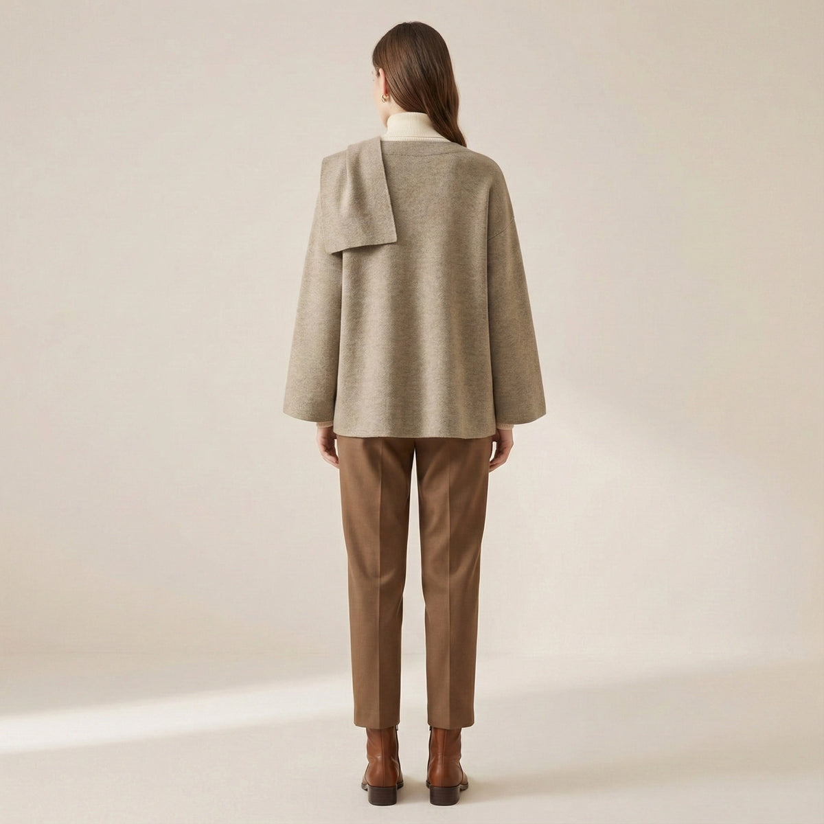 Woman wearing a beige coat and brown pants on a plain background