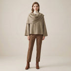Woman wearing a beige cape over a white turtleneck and brown pants on a beige background