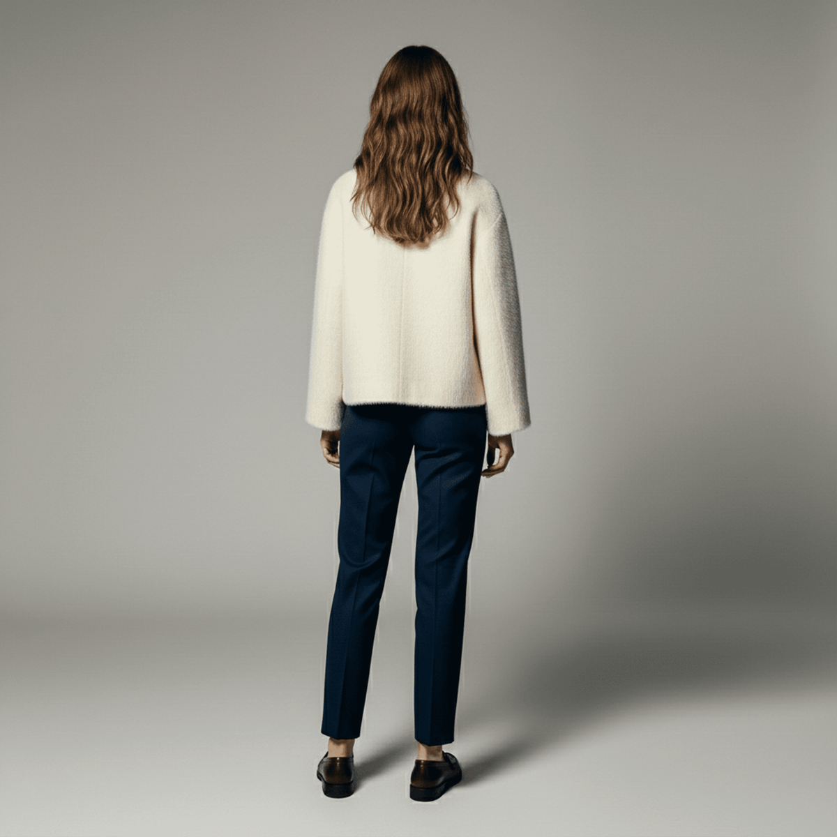 Person wearing a cream sweater and dark pants on a gray background